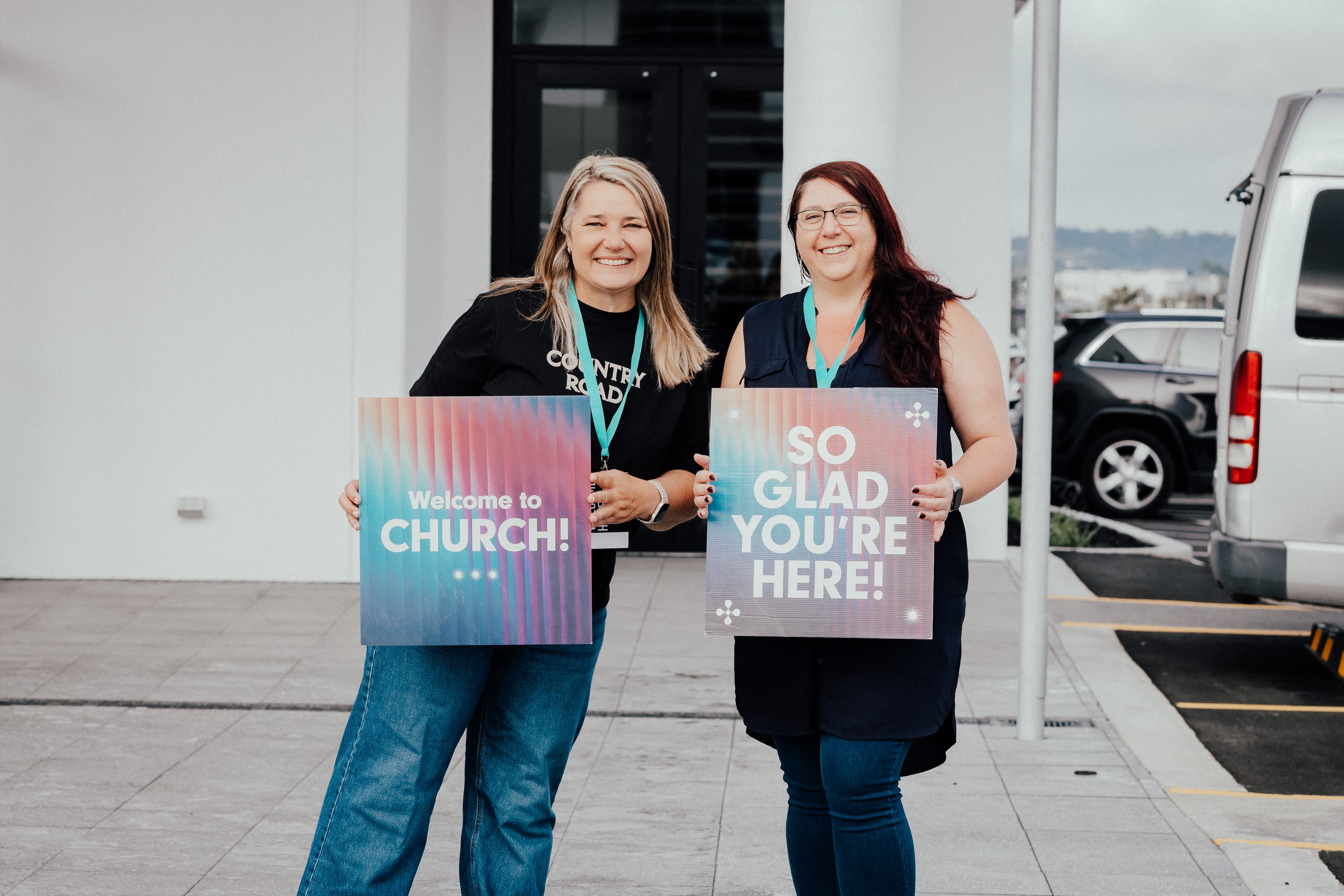 Two women standing outside LIFE North holding welcome signs and smiling at the camera