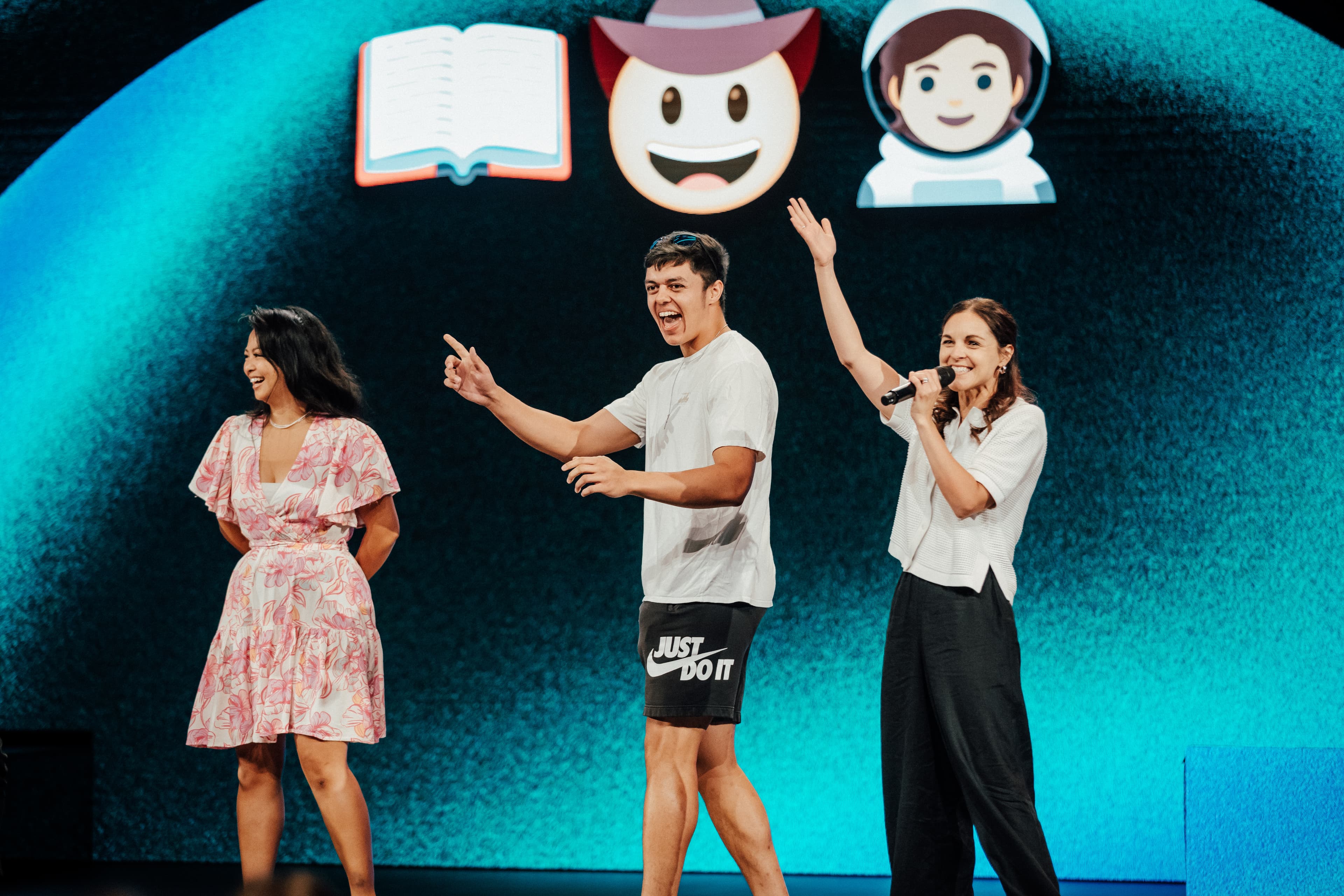Three people on stage playing an emoji guessing game on the screen behind them
