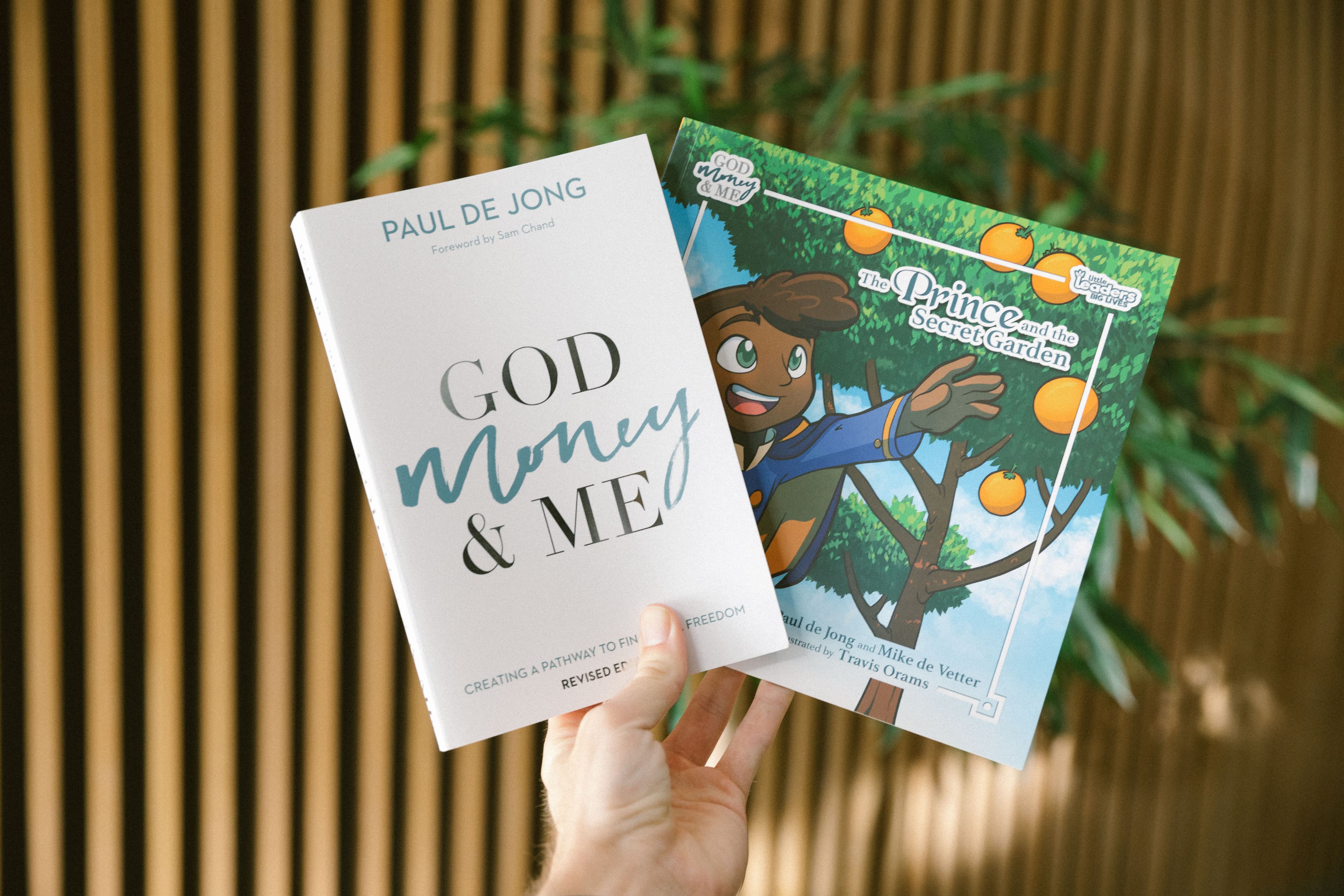 Hand holding God Money & Me and The Prince and the Secret Garden books by Ps Paul de Jong