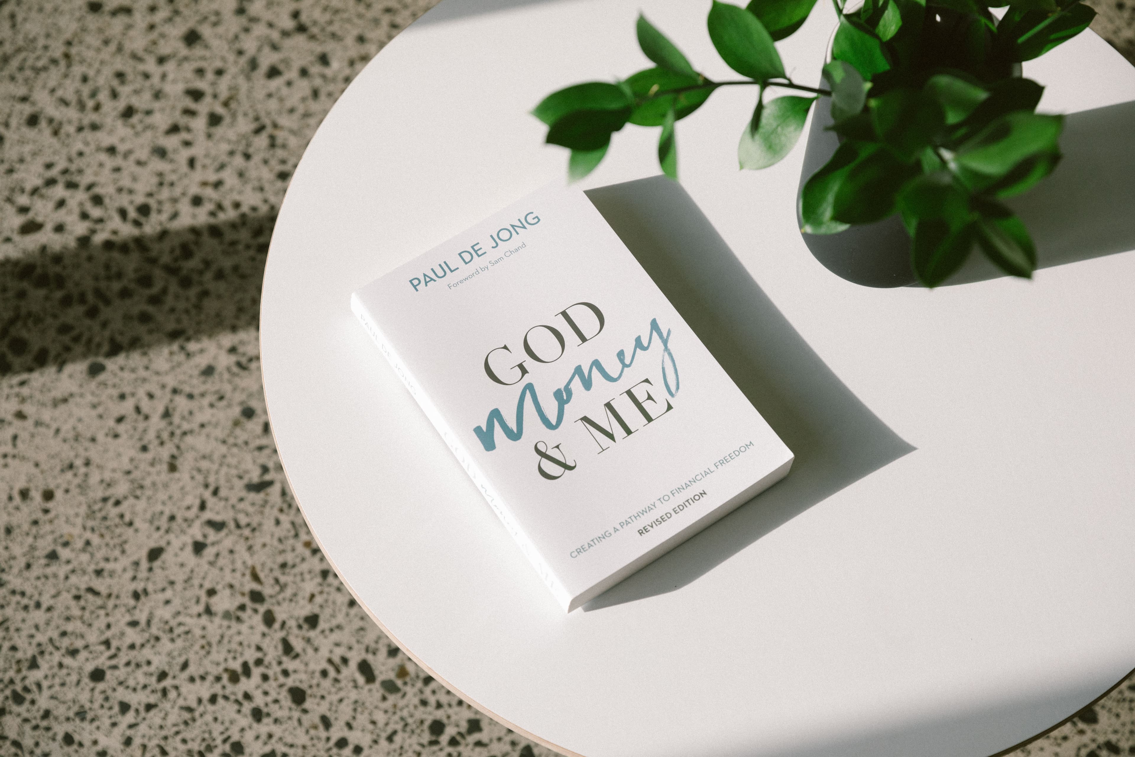 God, Money and Me book sitting on a coffee table with a vase of greenery next to it