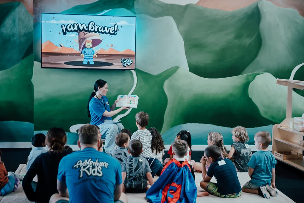 Person reading a book to a group of kids sitting down in Kids' Church