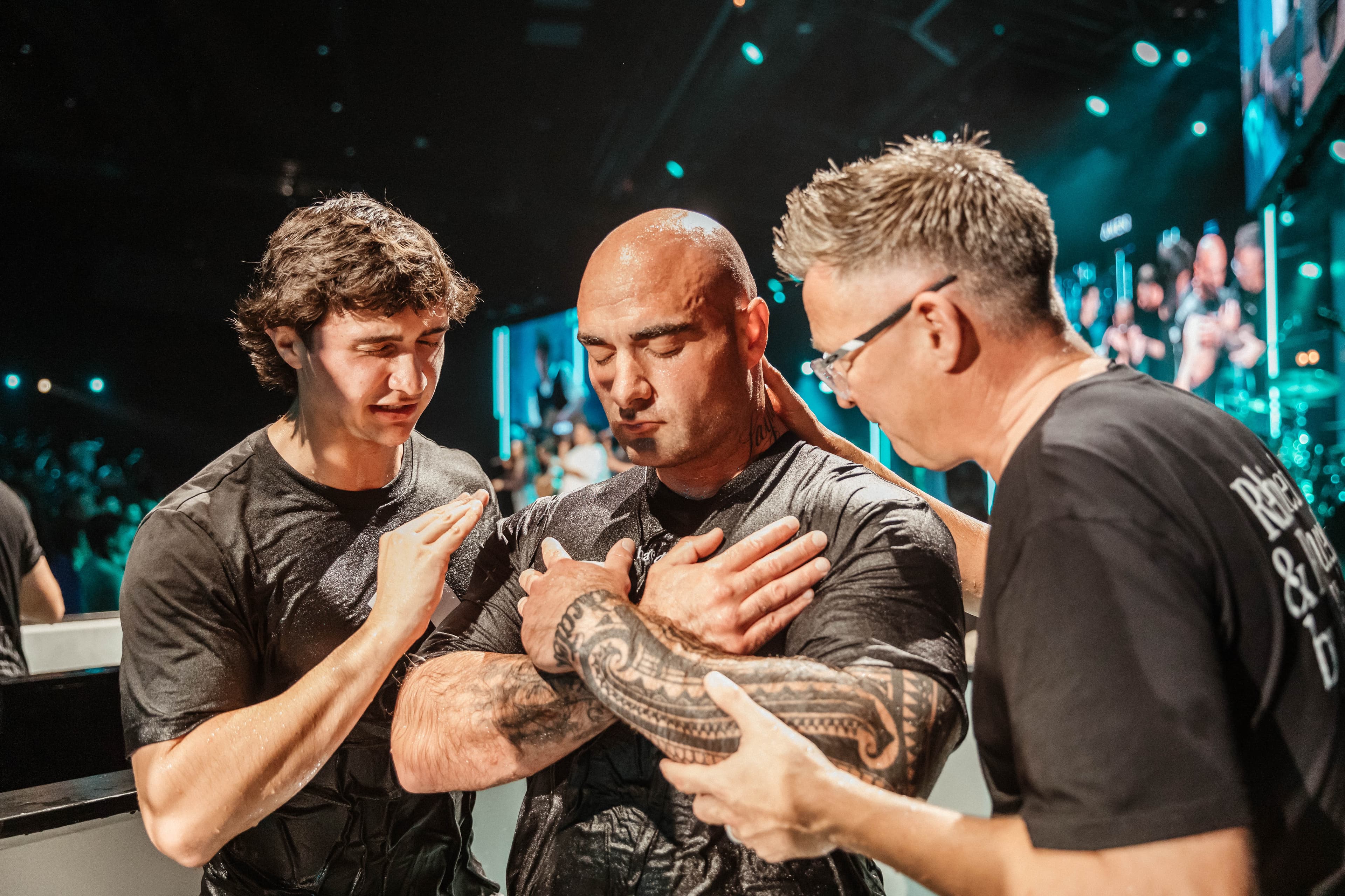 Man after he has been baptised with two men either side of him praying for him