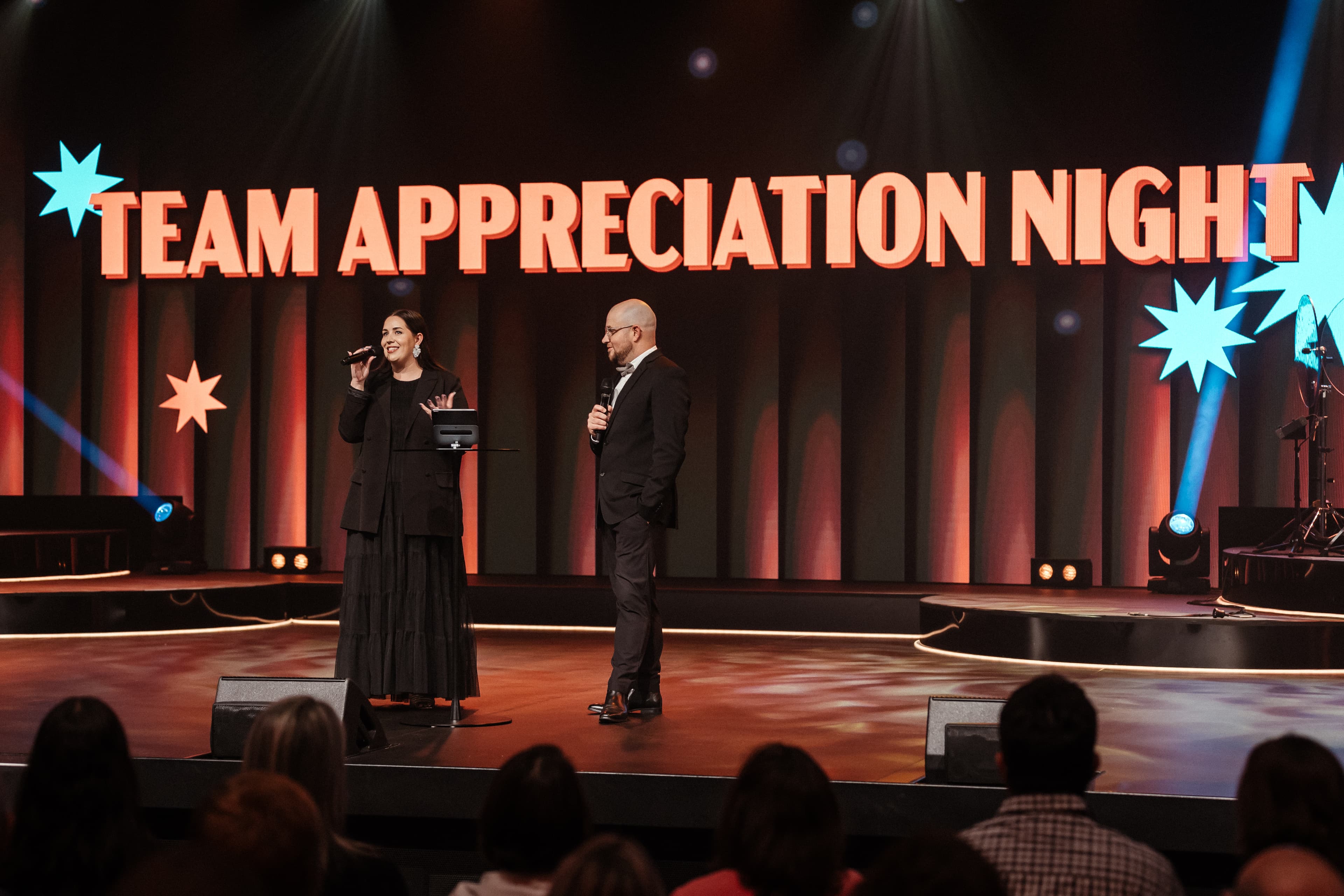 Ps Luke and Missy standing on stage with Team Appreciation Night on screen behind them