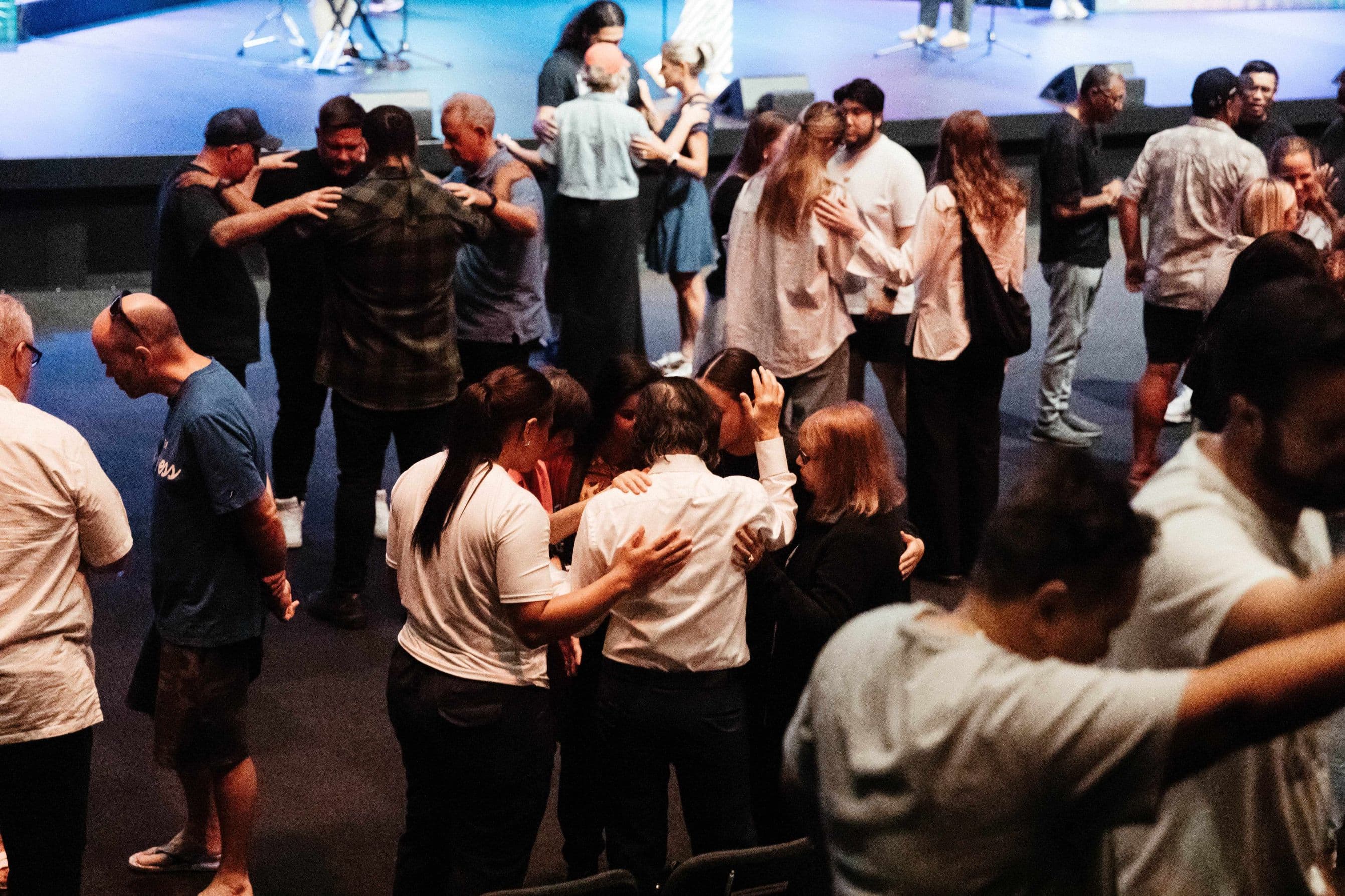 Lots of small groups of people praying together, some with hands on each other's backs at Central campus prayer meeting