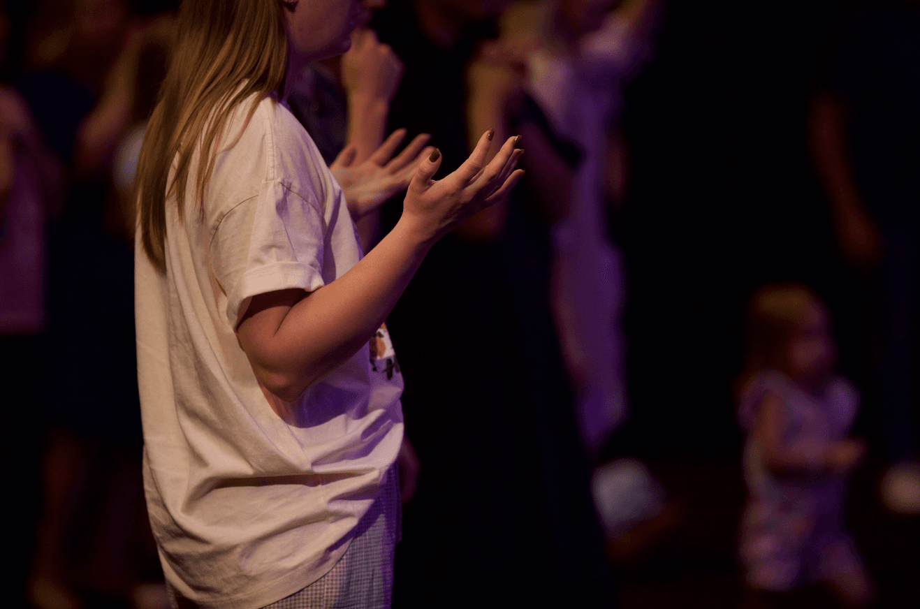 Woman from the side with her hands raised in front of her in worship during a prayer meeting