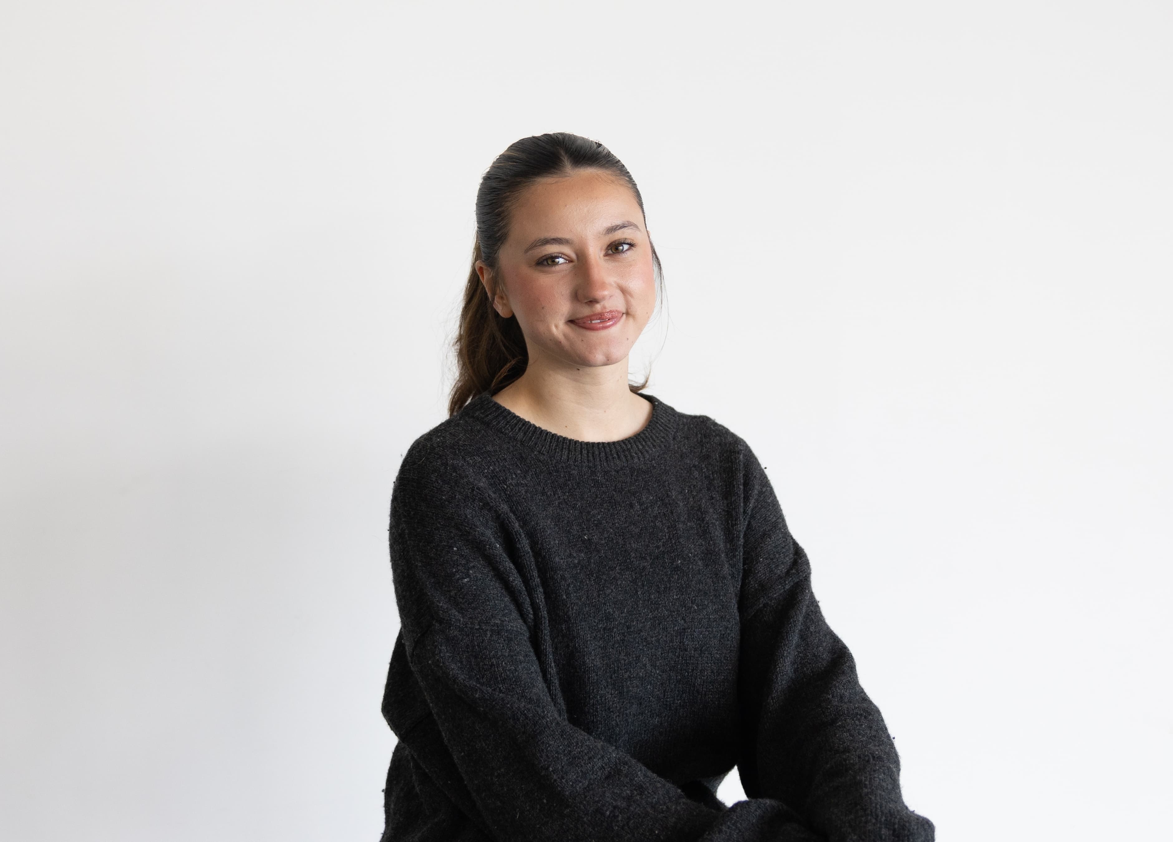 Cayla smiling at the camera while sitting on a stool with white background