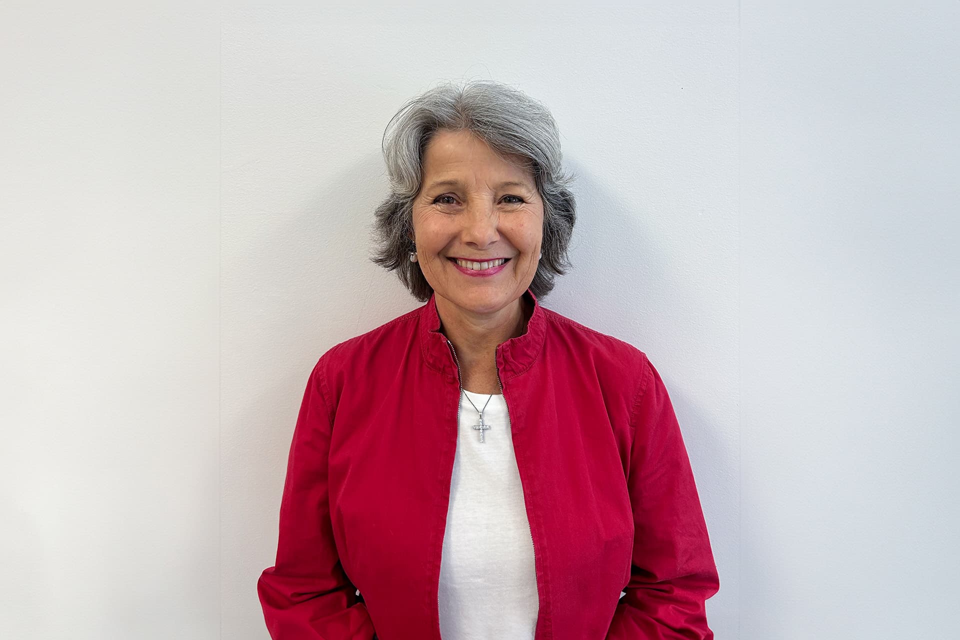 Robyn in a red jacked and white shirt against a white background smiling at the camera